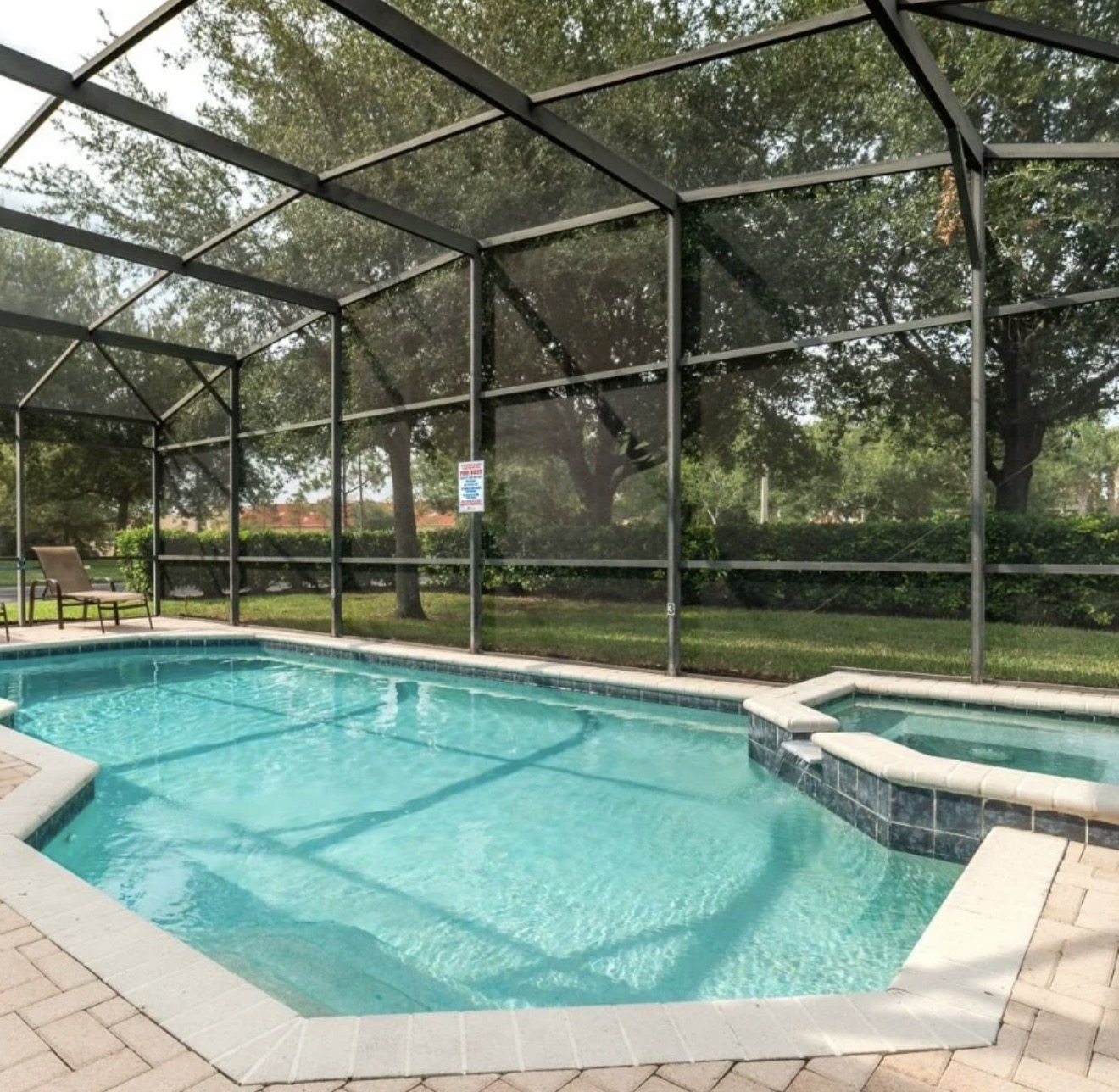 Screen-enclosed pool and spa surrounded by mature oaks